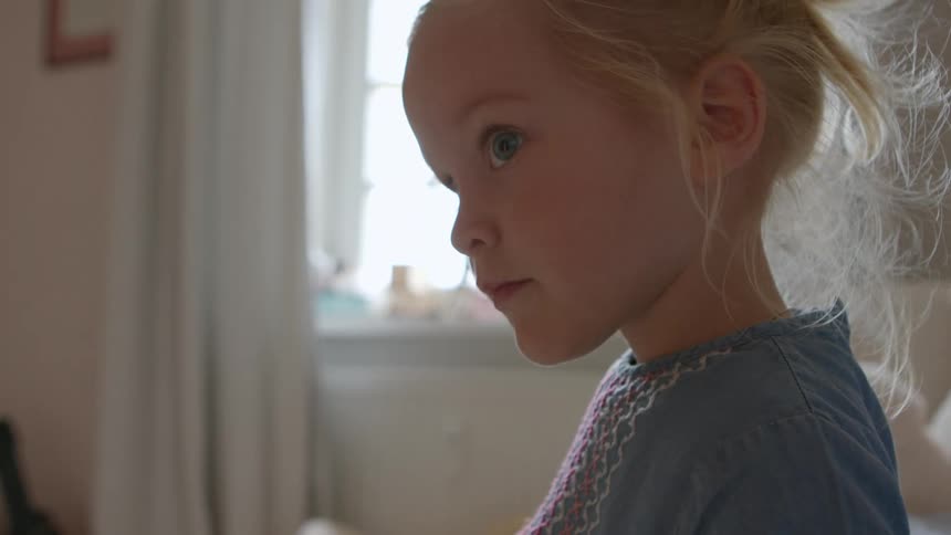 A young blonde caucasian girl stands in a bedroom and and looks up at something