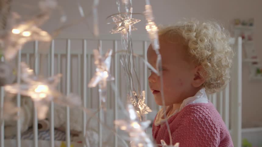 A little boy smiling and playing with some star shaped lights in a baby room