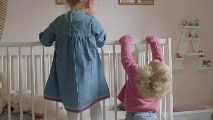 Two toddler girls hold on to the side of a crib and try to climb up