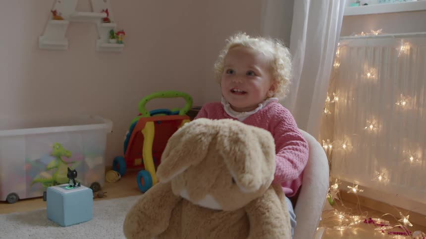 A young toddler girl sits on a large stuffed rocking chair and rocks back and forth
