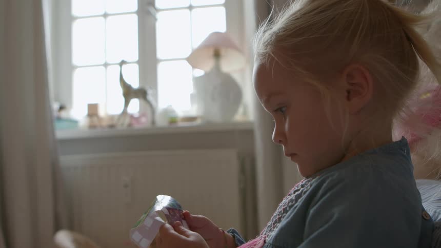 Little girl playing with a roll of stickers at daytime in her room
