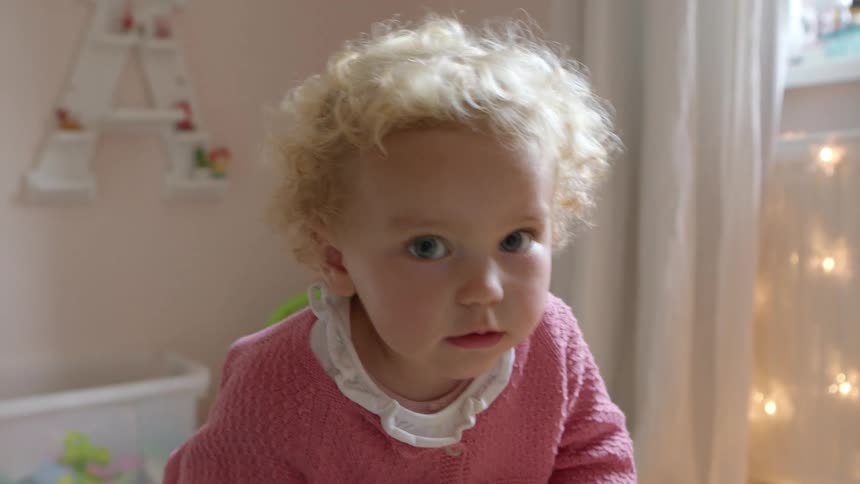 Baby girl plays walks and looks around in a nursery