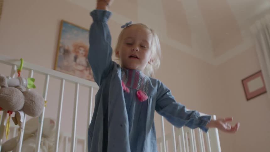 Little girl playing with bubbles inside of a babys room in front of a crib at daytime