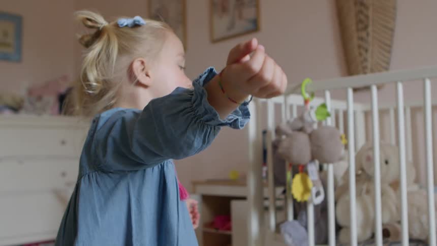 A young girl in a childs bedroom tosses a small stuffed animal into the air and watches as it falls to the floor