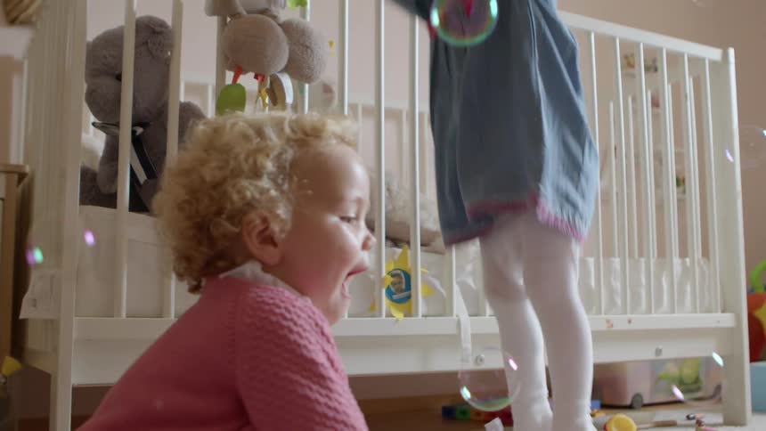 Two young toddler girls play with bubbles in their room