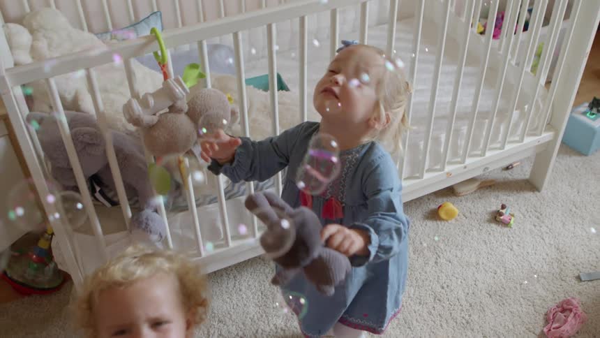 Girls playing with bubbles in a bedroom next to a cradle