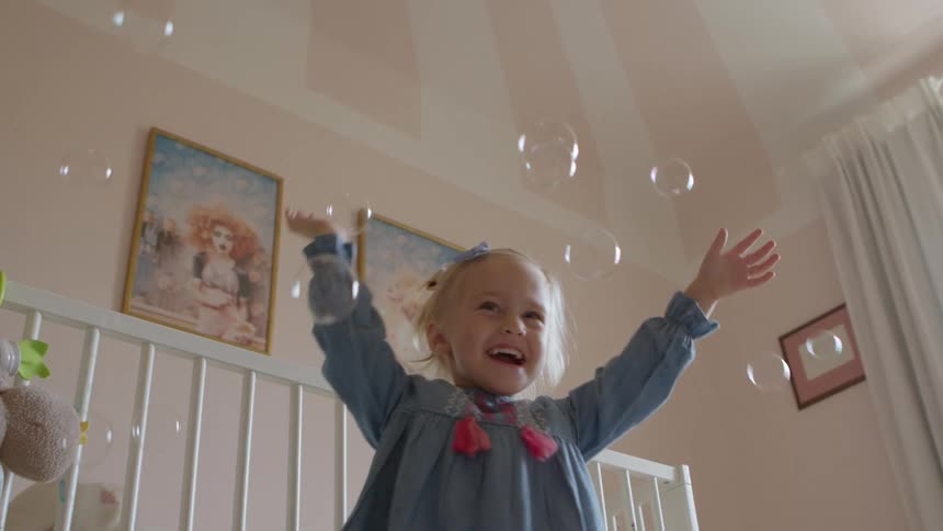 Two girls play with bubbles in a bedroom