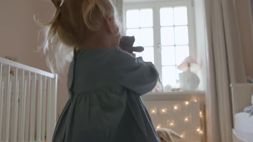 Small girl wearing a dress playing with a teddy bear in her room at home