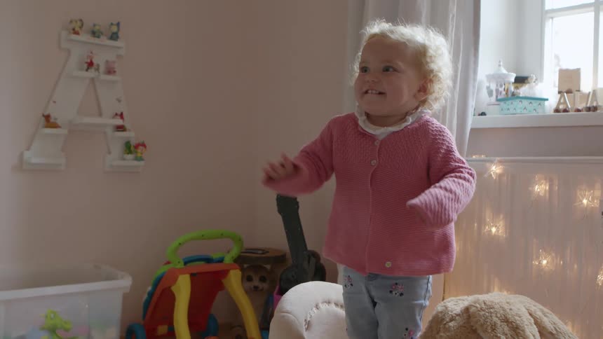 A blonde little girl stands on a rocking toy in a pink playroom balancing herself