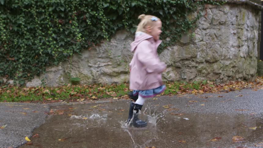 Little blonde girl running through a puddle in rain boots