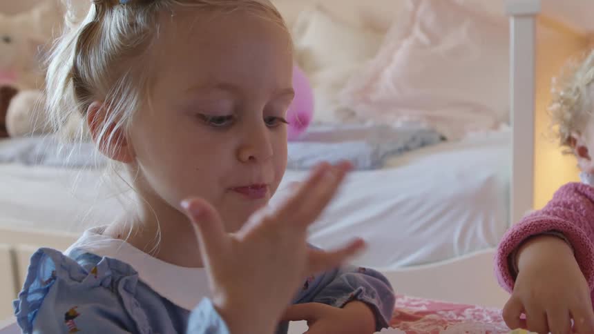 Two girls sit at a table eating while one child licks her fingers