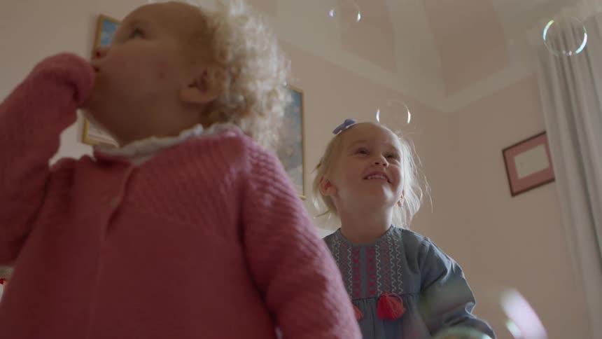 Young siblings laugh and jump around while playing with bubbles at home