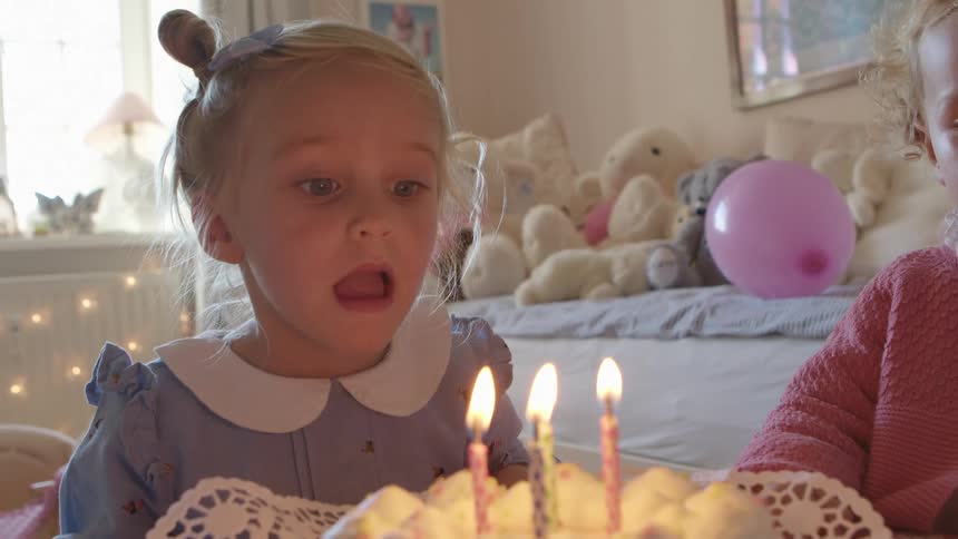 A young toddler girl attempts to out birthday candles