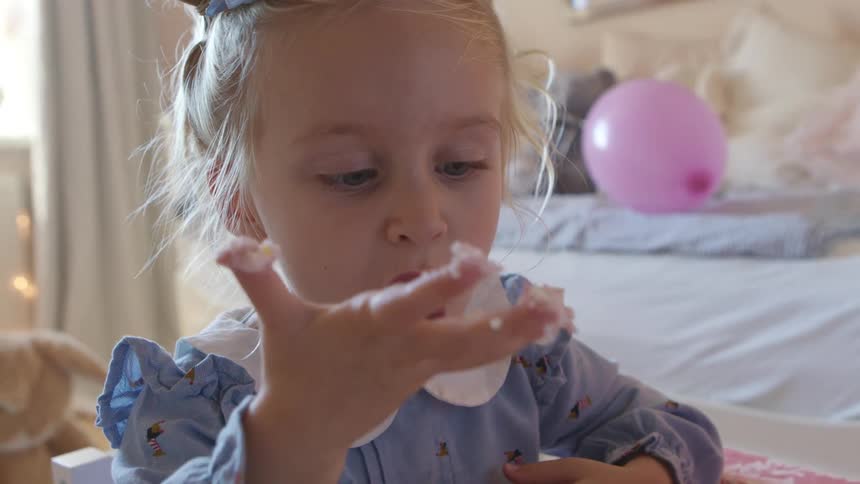 A young girl sits in her room and likes icing off of her fingers