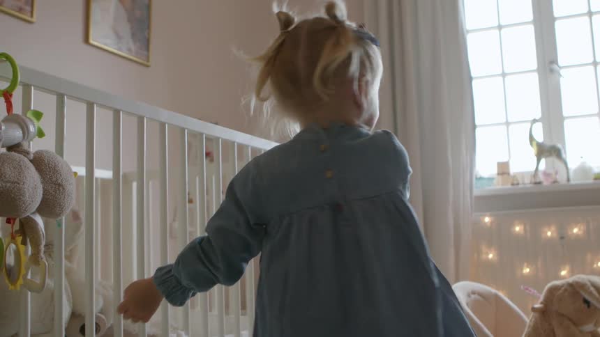 A young toddler girl spins in circles in her room then falls down