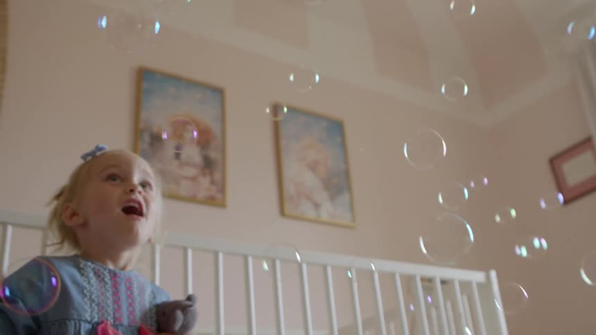 Two small children playing with bubbles in a bedroom
