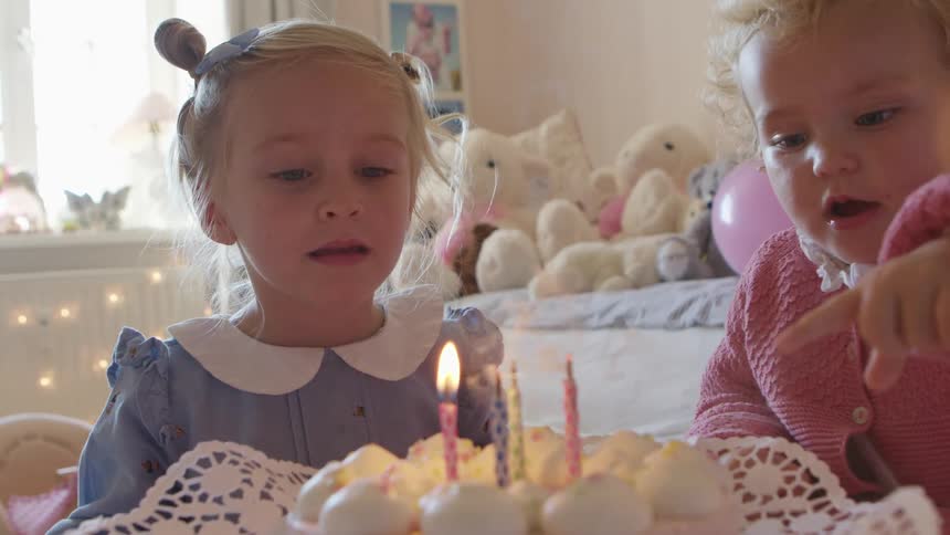 Little girl tries to the candles on a birthday cake in her room at home