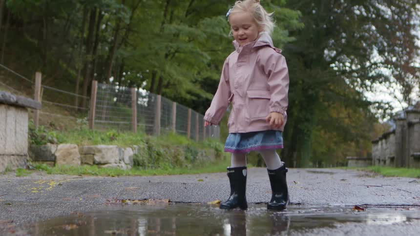 Little blonde girl happily jumping into a puddle