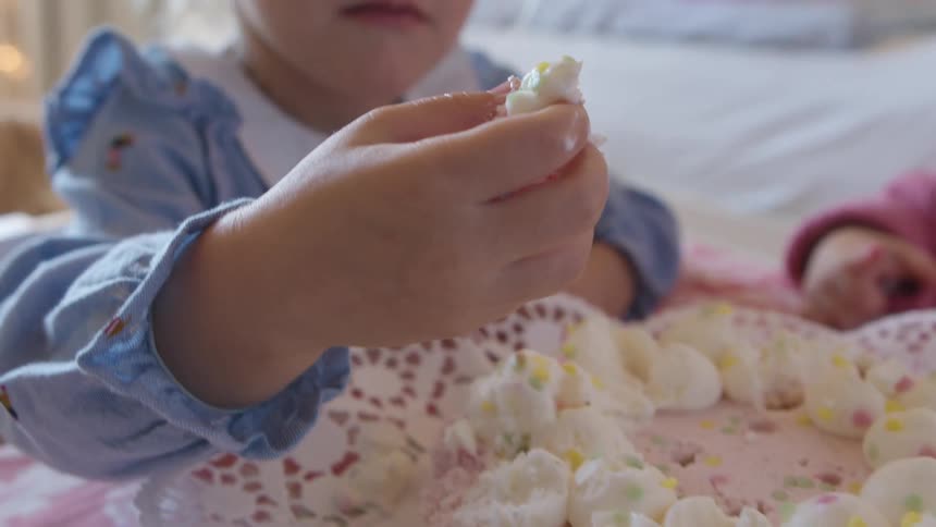 Girl uses fingers to pick and eat the icing and cream of a cake in a room at home