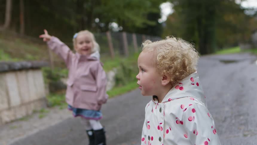 A little girl on a street in a neighborhood points and her younger sister turns and looks