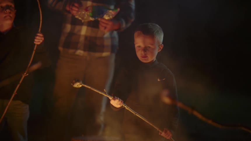 Boy and family roasting marshmallows over a campfire at night