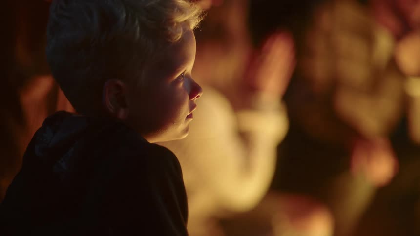Boy looking around sitting next to a group of people outside at night time
