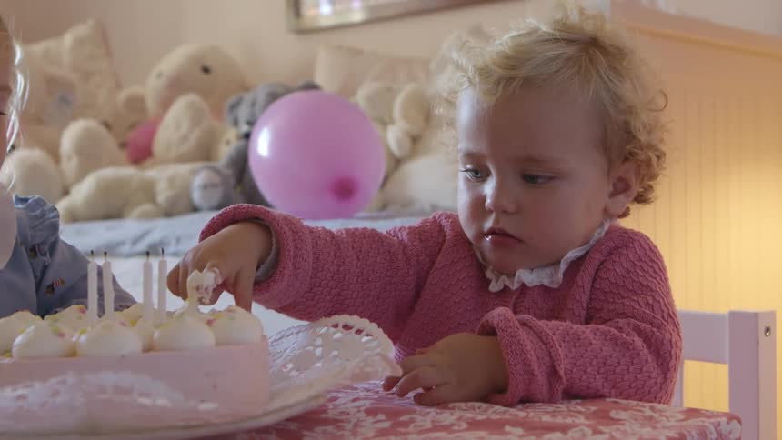 A toddler dips her finger in deviled eggs as she and her sister sit and eat in a playroom