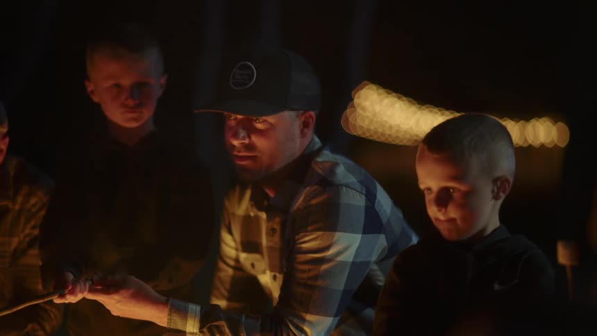 Two boys and two men sitting around a campfire roasting marshmallows on a stick