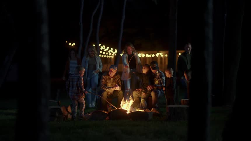 Family gathers around a campfire to roast marshmallows at night