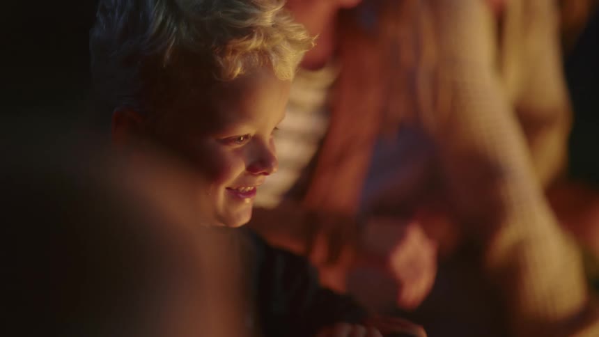 Small blonde boy smiling and having fun in a campfire with his family at night