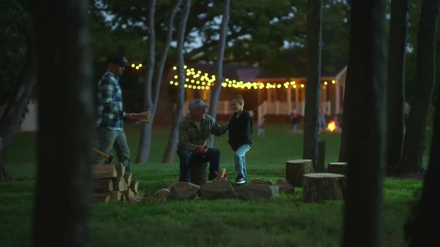 Two men build a campfire with a young boy standing beside them