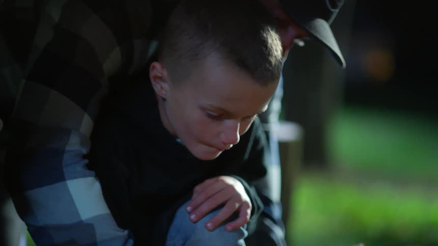 A man holds his son while helping him light a fire outside