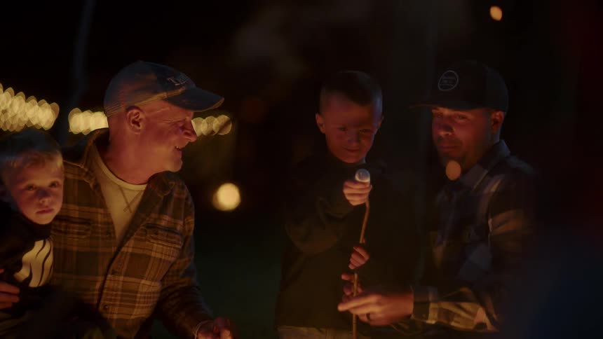Two men and two children around a camp fire roasting marshmellows
