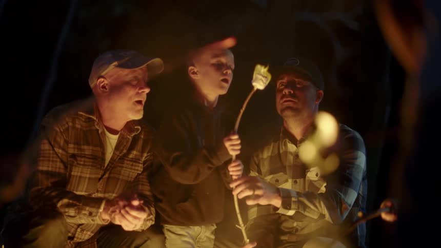 A group of people sitting around the campfire roasts marshmallows