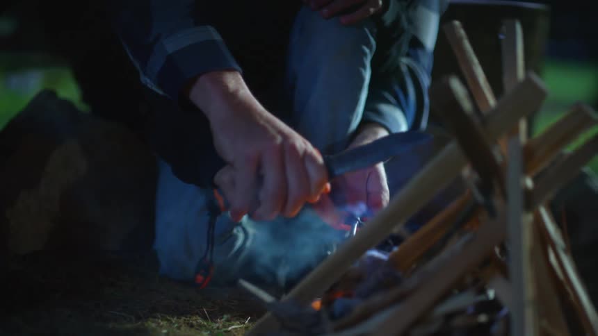 Father holding his sons hands from behind helping him start a small campfire
