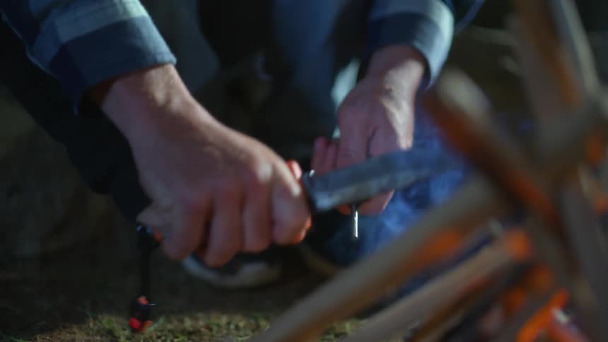 Hands striking a knife across a small metal stick trying to start a fire