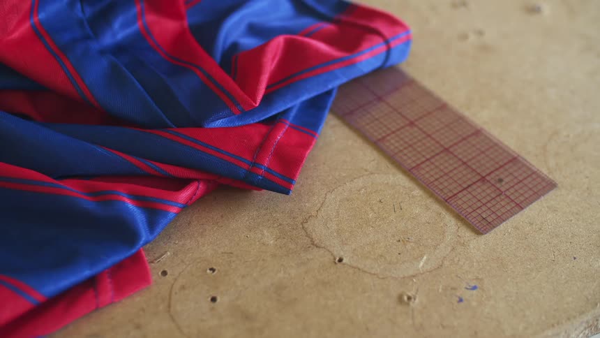 A red and blue striped shirt on a wooden table next to a measuring stick