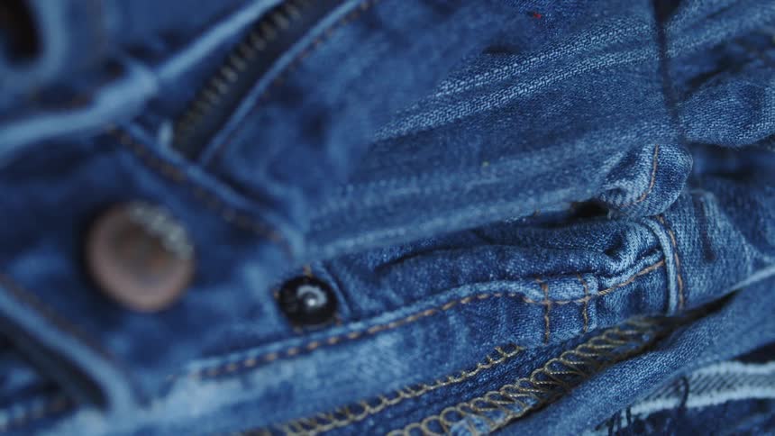 A piece of denim that is sitting idly has precise stitches and a zipper idly
