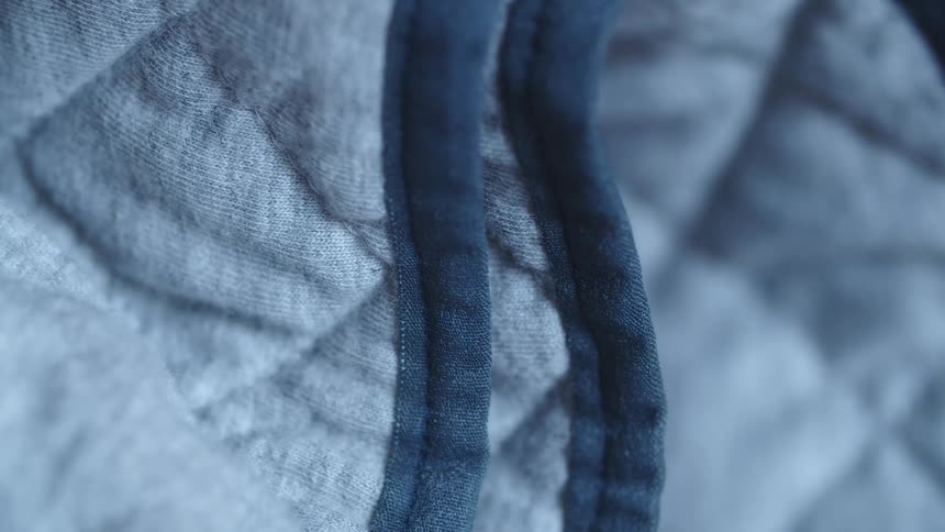A piece of fabric has squared stitching and a dark trim on its edge