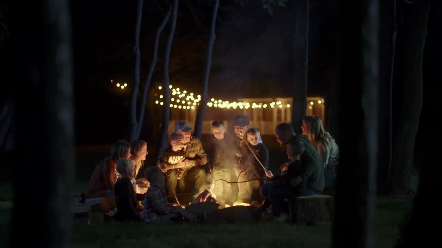 A group of people sitting around the campfire roasts marshmallows