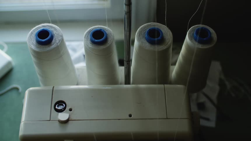 A sewing machine with four spools of white thread all on a table in front of a window