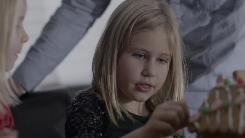 Two young girls play with a gingerbread house
