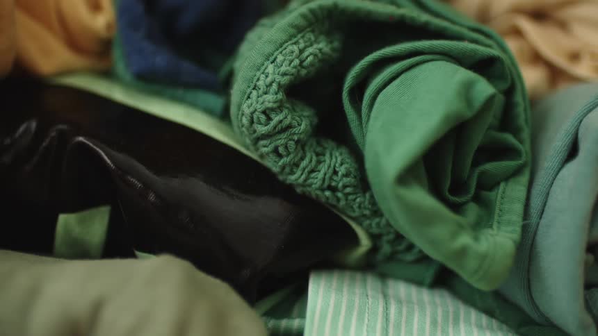 Colorful throws and blankets sit rolled up and piled up on a bed