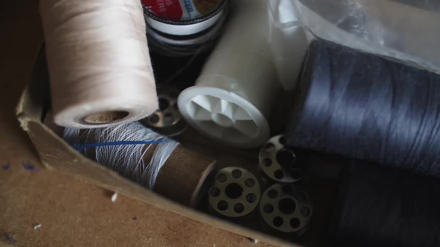 A box containing several spools of thread on a carpeted floor