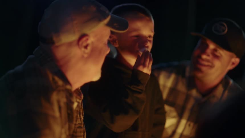 Boy eating marshmallows in front of a campfire with his father and grandfather