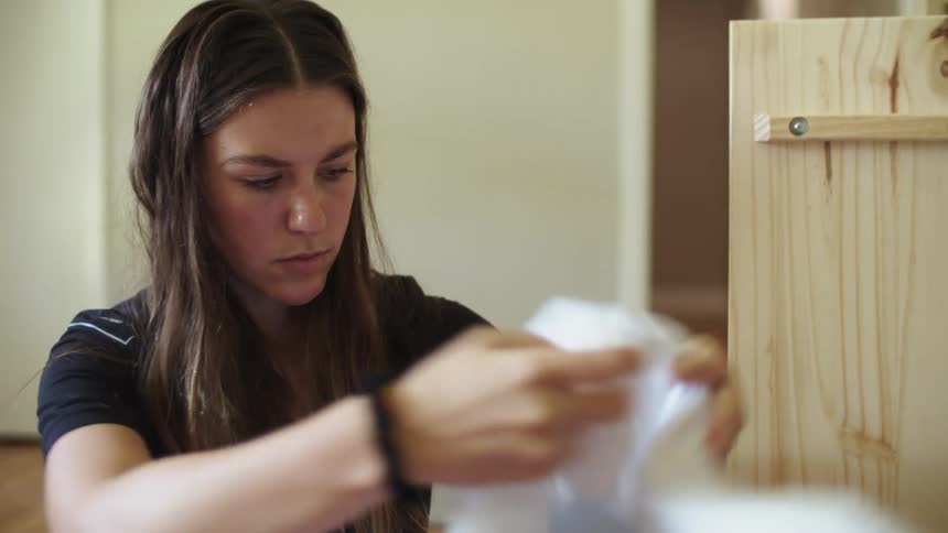 A young woman sitting in a room indoors examines a white sports jersey before putting it away