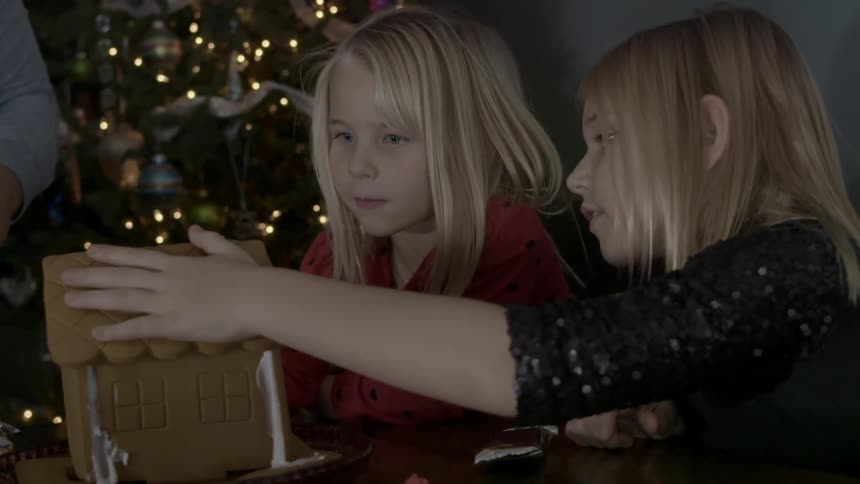 Two girls place a roof on a gingerbread house