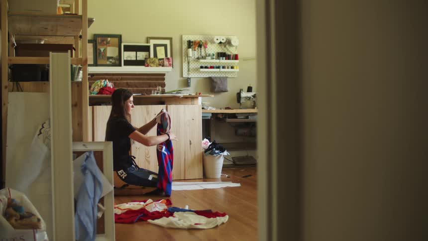 Woman knelt down on a hardwood floor folding a jersey shirt in a sewing craft workshop