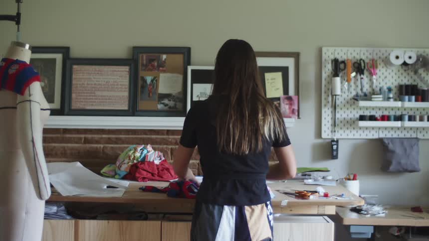 A woman stands in her sewing rom and unfolds a piece of red and blue striped fabric