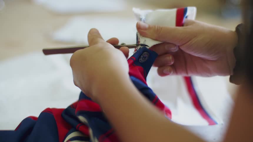 A woman uses an arched stitch remover on thread to separate pieces of fabric